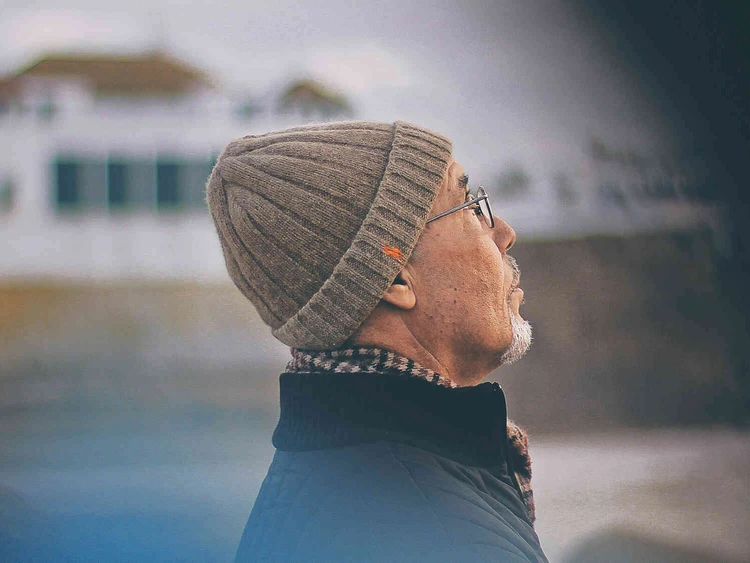 Nahaufnahme von einem &auml;lteren Mann mit einer M&uuml;tze drau&szlig;end stehend und in die ferne schauend